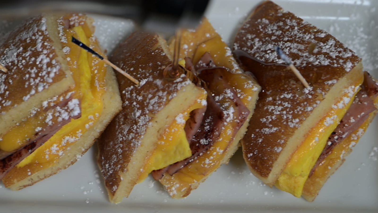 Three monte cristo sandwiches dusted with powdered sugar, plated on a white platter